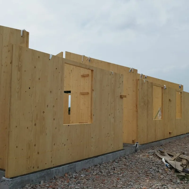 Casa in legno moderna con facciata naturale, grandi vetrate e luce calda.