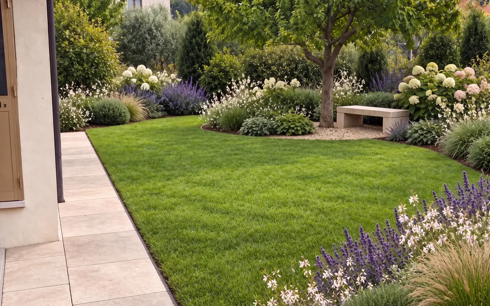 Giardino residenziale rinnovato con prato curato, bordure fiorite e pavimentazione perimetrale in pietra.